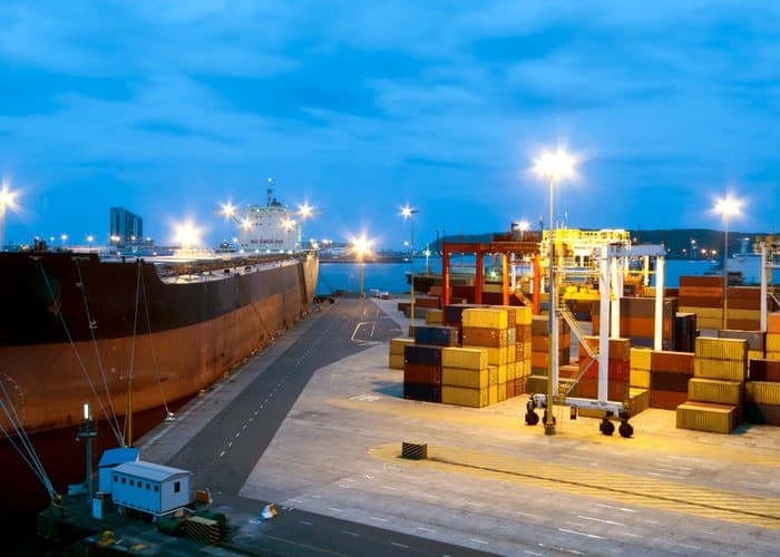 Container port at dusk with a cargo ship at the wharf and stacked shipping containers