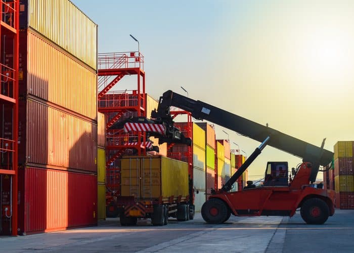 Reach stacker lifting a shipping container onto a truck in a container yard
