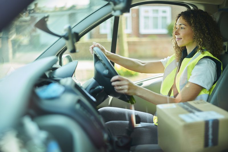 Woman driver in a hi-vis vest at the wheel of a delivery van
